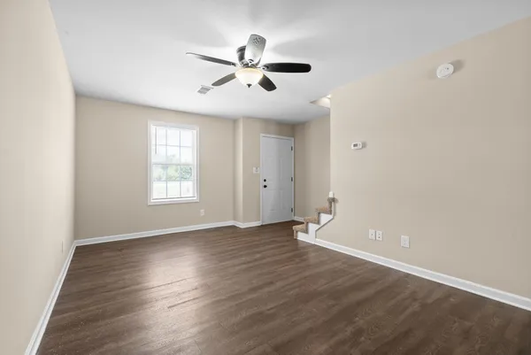 an empty room with wooden floor chandelier fan and windows