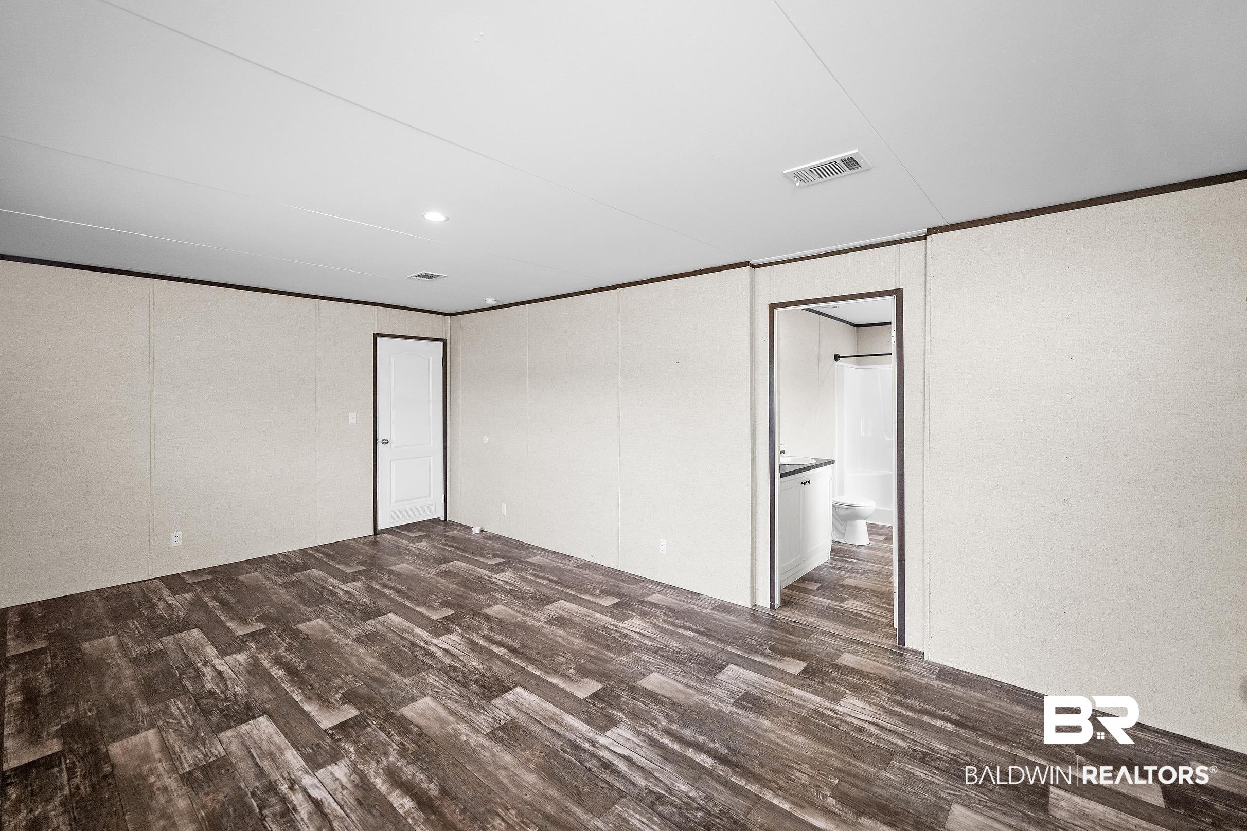 21601 Westside Loop Silverhill, AL 36576 - Photo 19 of 42 Spacious room featuring wood-finish flooring, light-toned wall panels, and dark trim