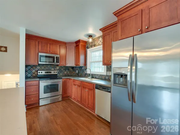 a kitchen with stainless steel appliances granite countertop a refrigerator a stove and a sink with wooden floor