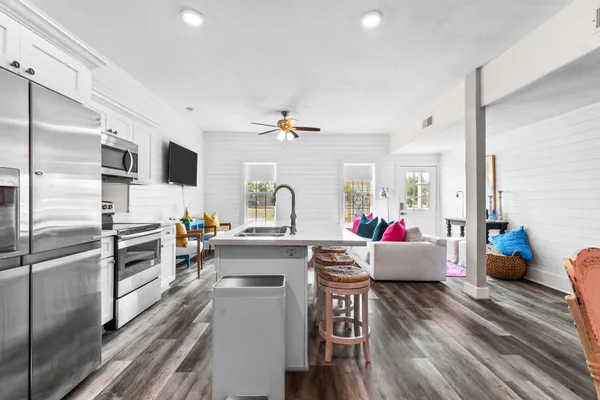 a kitchen with stainless steel appliances kitchen island granite countertop a refrigerator a stove top oven a dining table and chairs with wooden floor