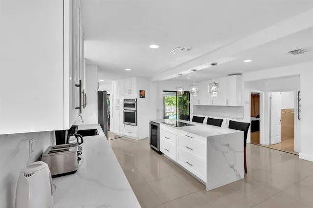 a large white kitchen with stainless steel appliances kitchen island a stove a refrigerator a couch and a dining table with wooden floor