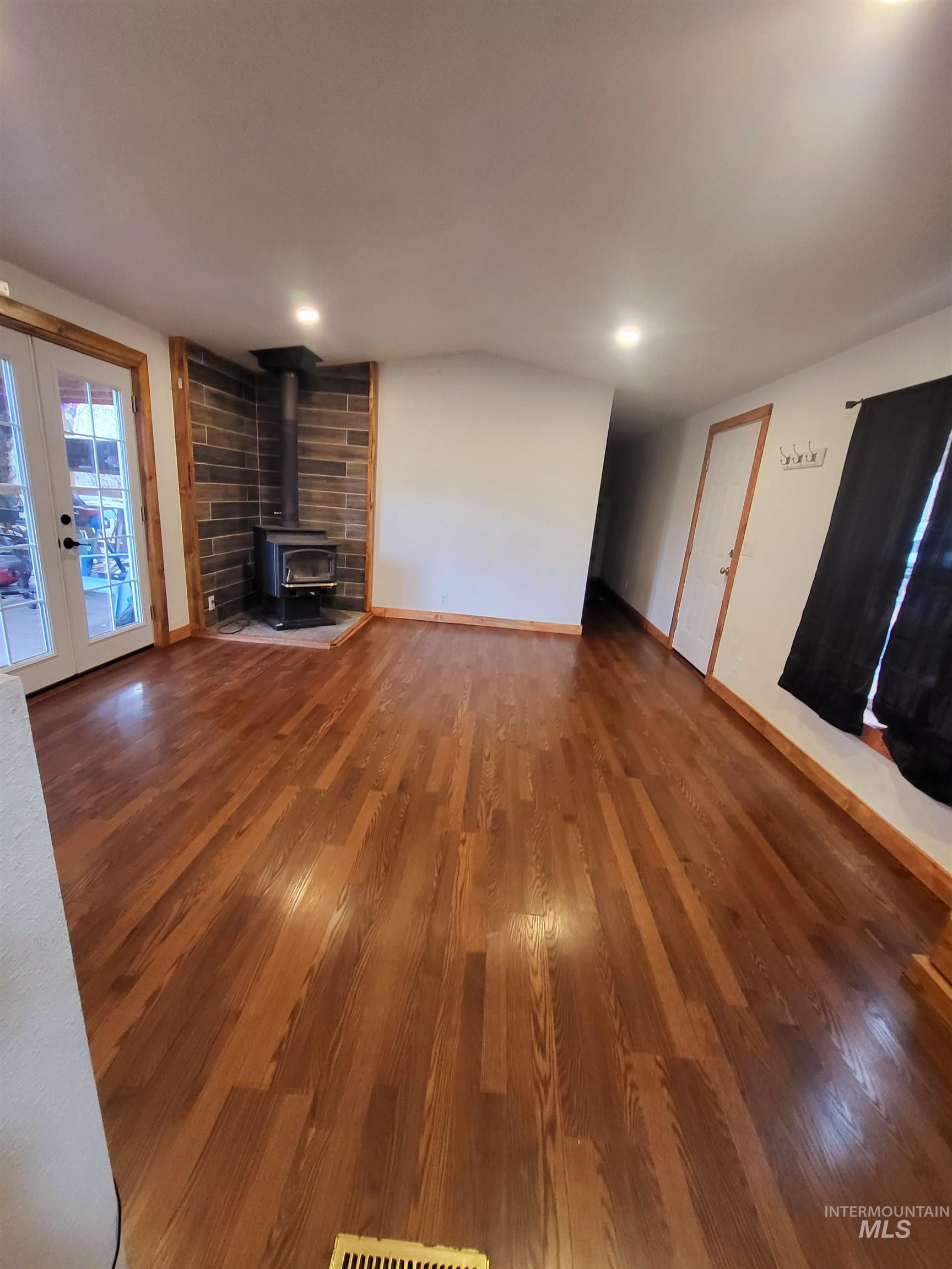 Unfurnished living room with wood finished floors, a wood stove, french doors, and recessed lighting