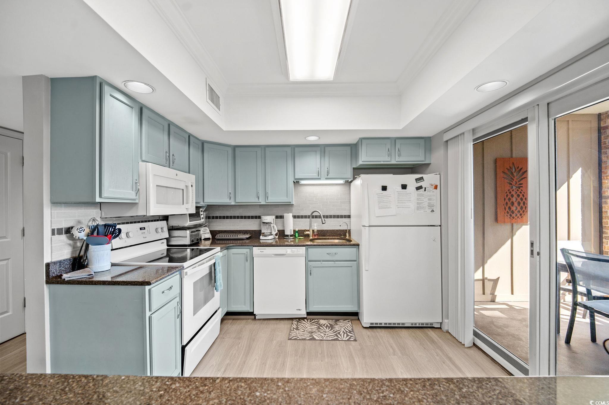 320 Myrtle Avenue Pawleys Island, SC 29585 - Photo 19 of 38 Kitchen with white appliances, tasteful backsplash, a tray ceiling, light wood-type flooring, and ornamental molding