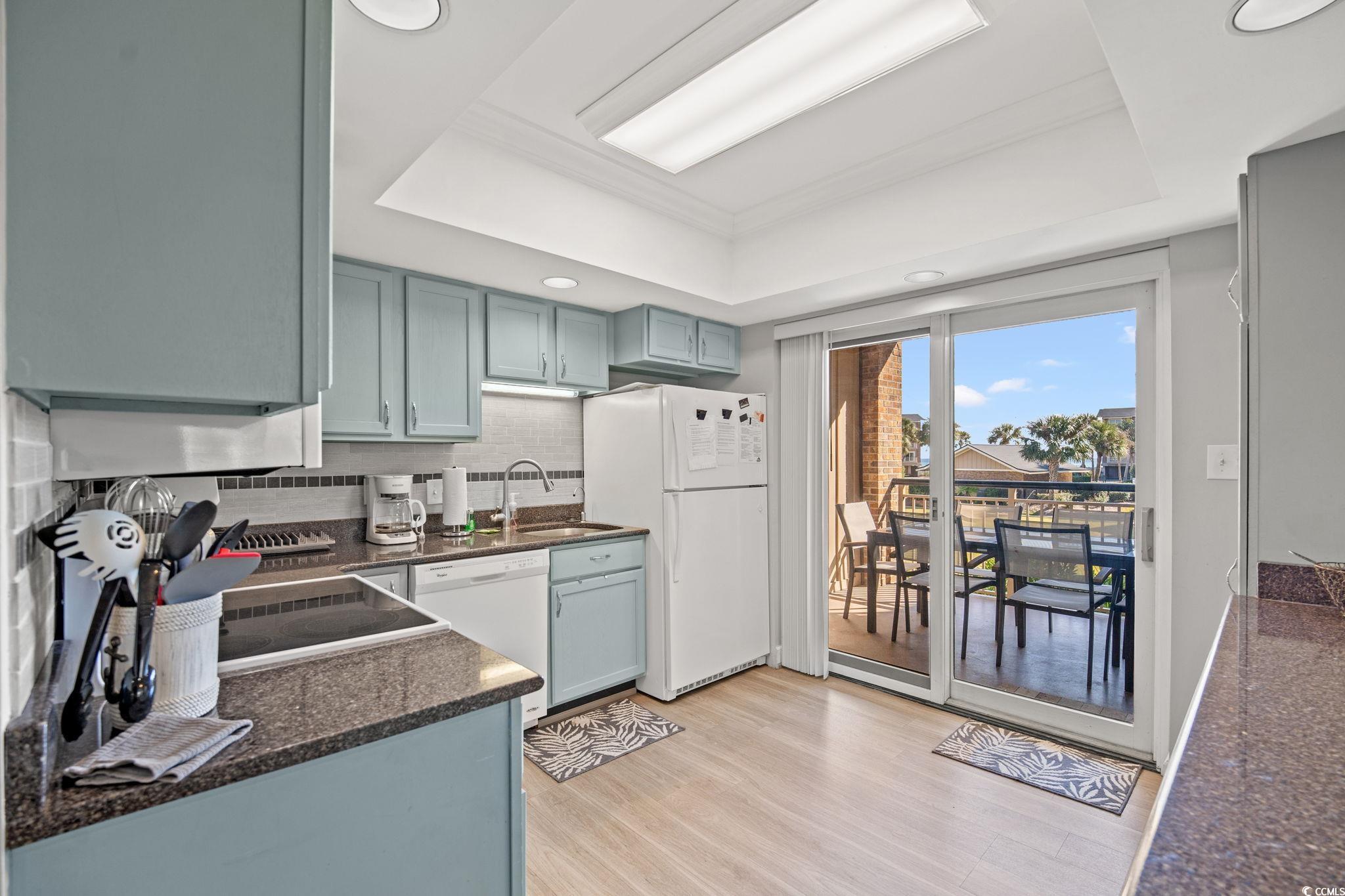 320 Myrtle Avenue Pawleys Island, SC 29585 - Photo 21 of 38 Kitchen featuring a tray ceiling, decorative backsplash, white appliances, light wood-style flooring, and dark stone counters