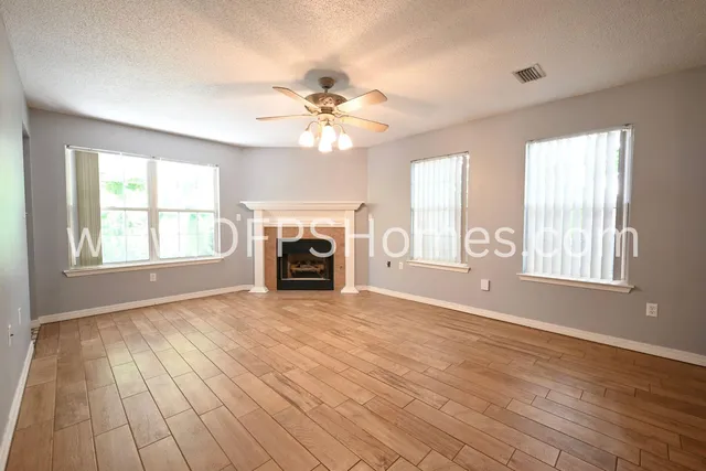 an empty room with windows fireplace and a ceiling fan