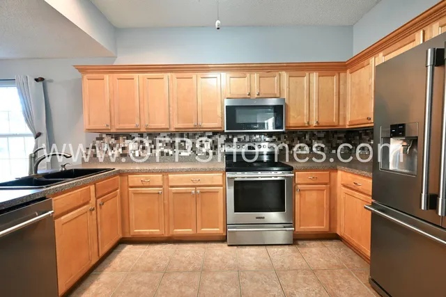 a kitchen with stainless steel appliances granite countertop a sink a stove a microwave a refrigerator and cabinets