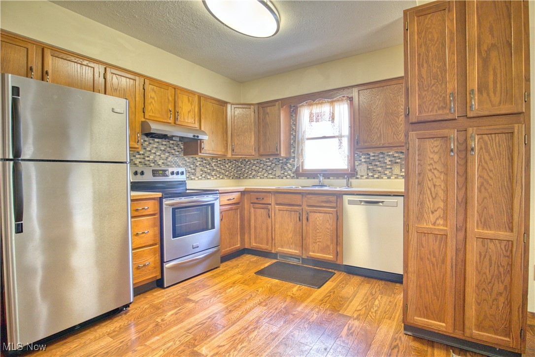 7017 Kirk Road Canfield, OH 44406 - Photo 30 of 35 Kitchen featuring appliances with stainless steel finishes, light wood-style flooring, decorative backsplash, a textured ceiling, and light countertops