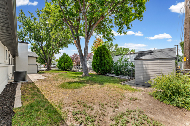 1898 West 600 South Provo, UT 84601 - Photo 32 of 32 Grassy backyard featuring mature trees, a detached storage shed with a shingled roof, and a paved walkway