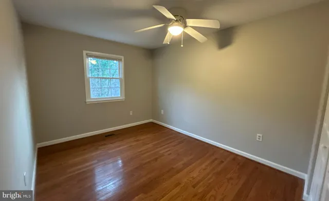 an empty room with wooden floor fan and windows