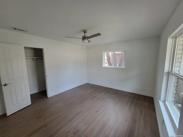 an empty room with wooden floor fan and windows