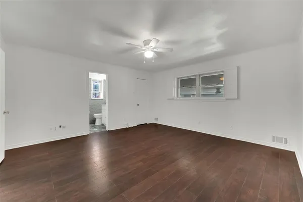 a view of an empty room with wooden floor and a ceiling fan