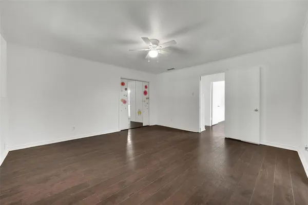 a view of an empty room with wooden floor and a ceiling fan