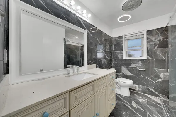 a bathroom with a sink vanity granite toilet and a mirror