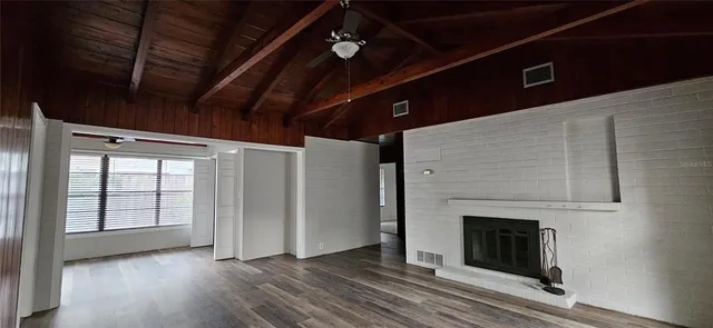 a view of an empty room with wooden floor fireplace and a window