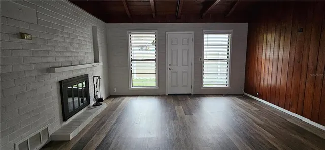 an empty room with wooden floor fireplace and windows