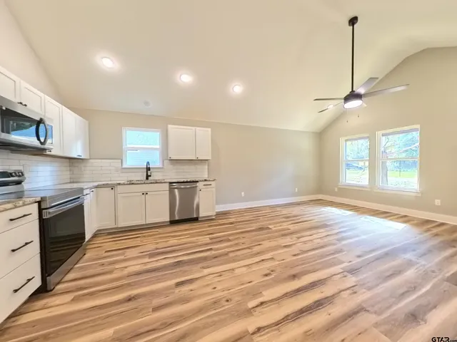 a large kitchen with stainless steel appliances granite countertop a stove a sink and white cabinets with wooden floor