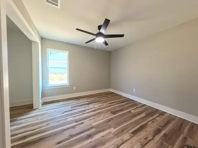 a view of empty room with wooden floor and fan
