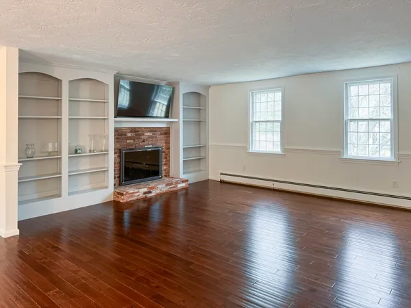 an empty room with wooden floor fireplace and windows