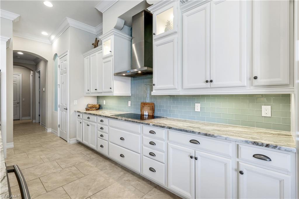 1456 Mockingbird Drive Naples, FL 34120 - Photo 11 of 43 Kitchen featuring white cabinets, arched walkways, light stone counters, wall chimney range hood, and backsplash