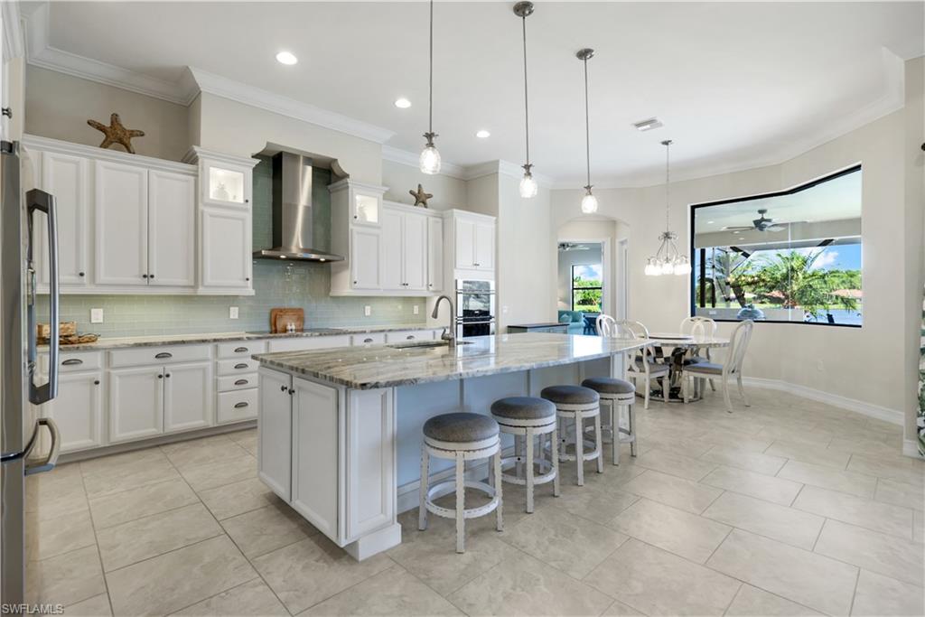 1456 Mockingbird Drive Naples, FL 34120 - Photo 12 of 43 Kitchen with light stone counters, ornamental molding, backsplash, stainless steel appliances, and wall chimney exhaust hood