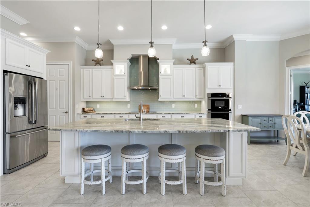 1456 Mockingbird Drive Naples, FL 34120 - Photo 8 of 43 Kitchen featuring stainless steel appliances, light stone countertops, white cabinets, crown molding, and a breakfast bar