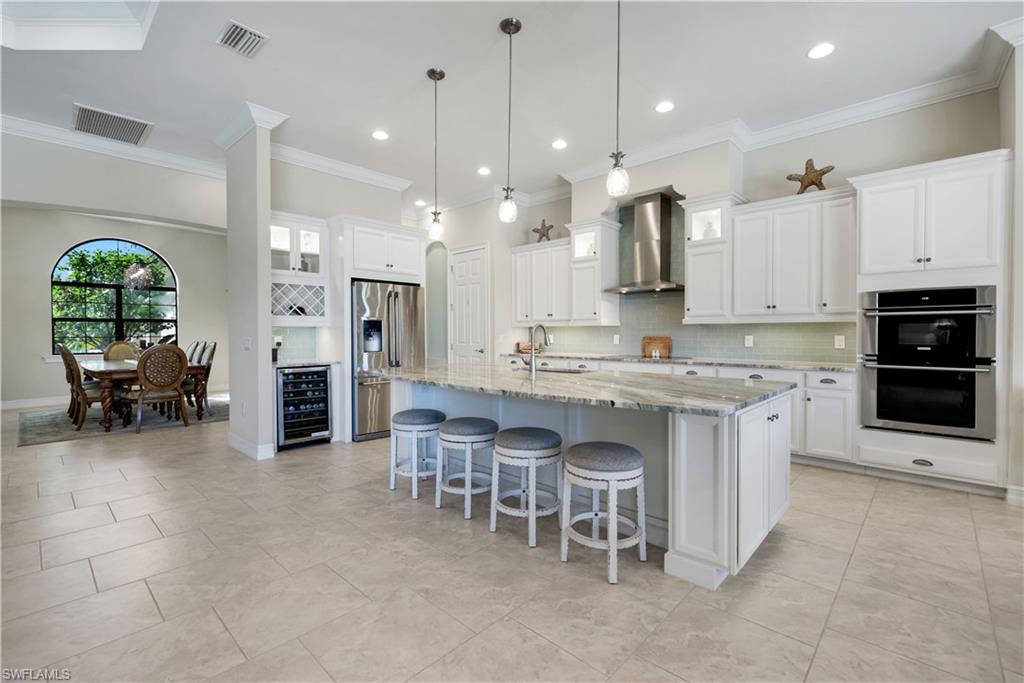 1456 Mockingbird Drive Naples, FL 34120 - Photo 9 of 43 Kitchen featuring backsplash, a kitchen breakfast bar, glass insert cabinets, stainless steel appliances, and light stone counters