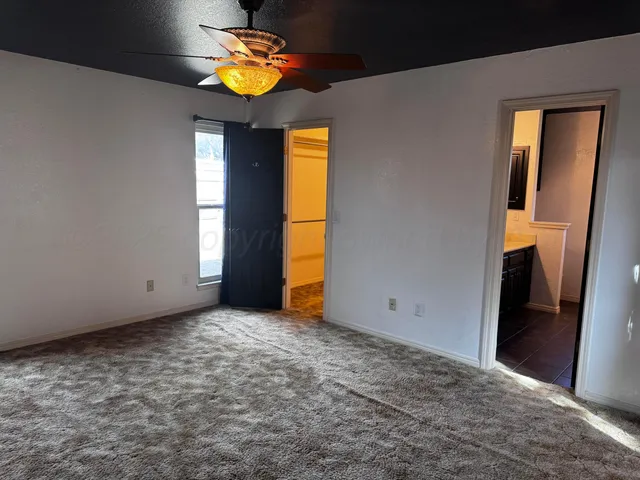 a view of an empty room with window and chandelier fan