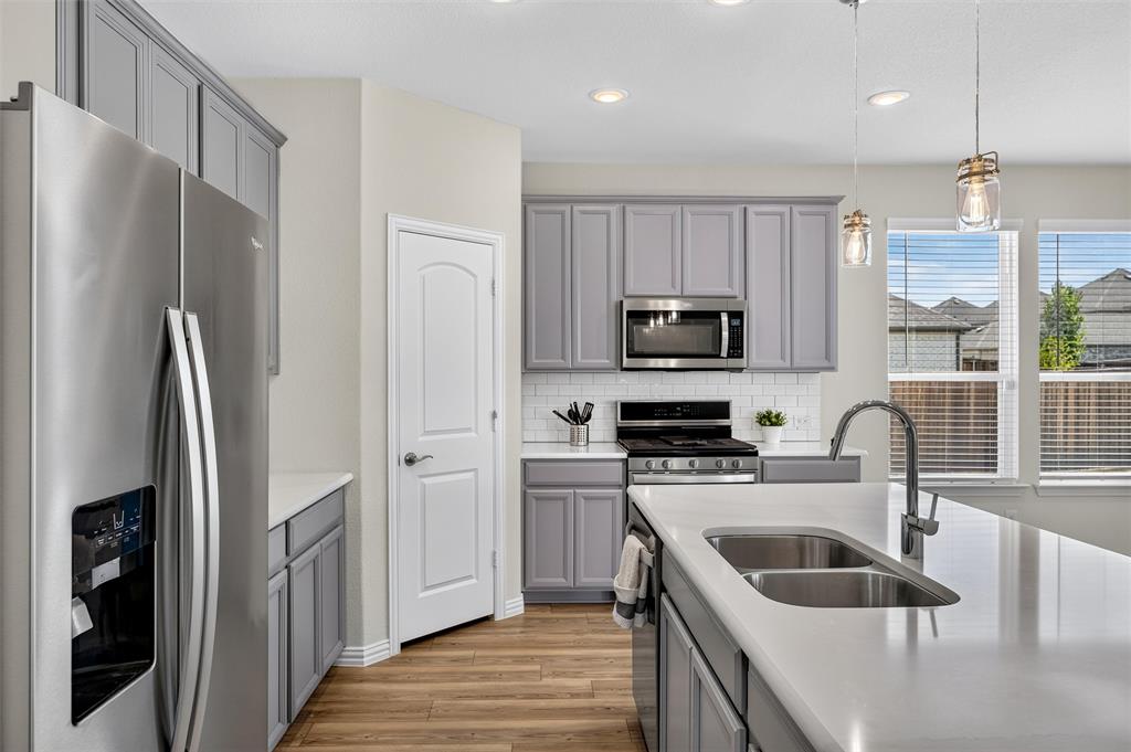 8715 Royal Star Road Rowlett, TX 75089 - Photo 18 of 39 Kitchen featuring wood-finish flooring, stainless steel appliances, gray cabinetry, white subway tile backsplash, and an island with a double basin sink