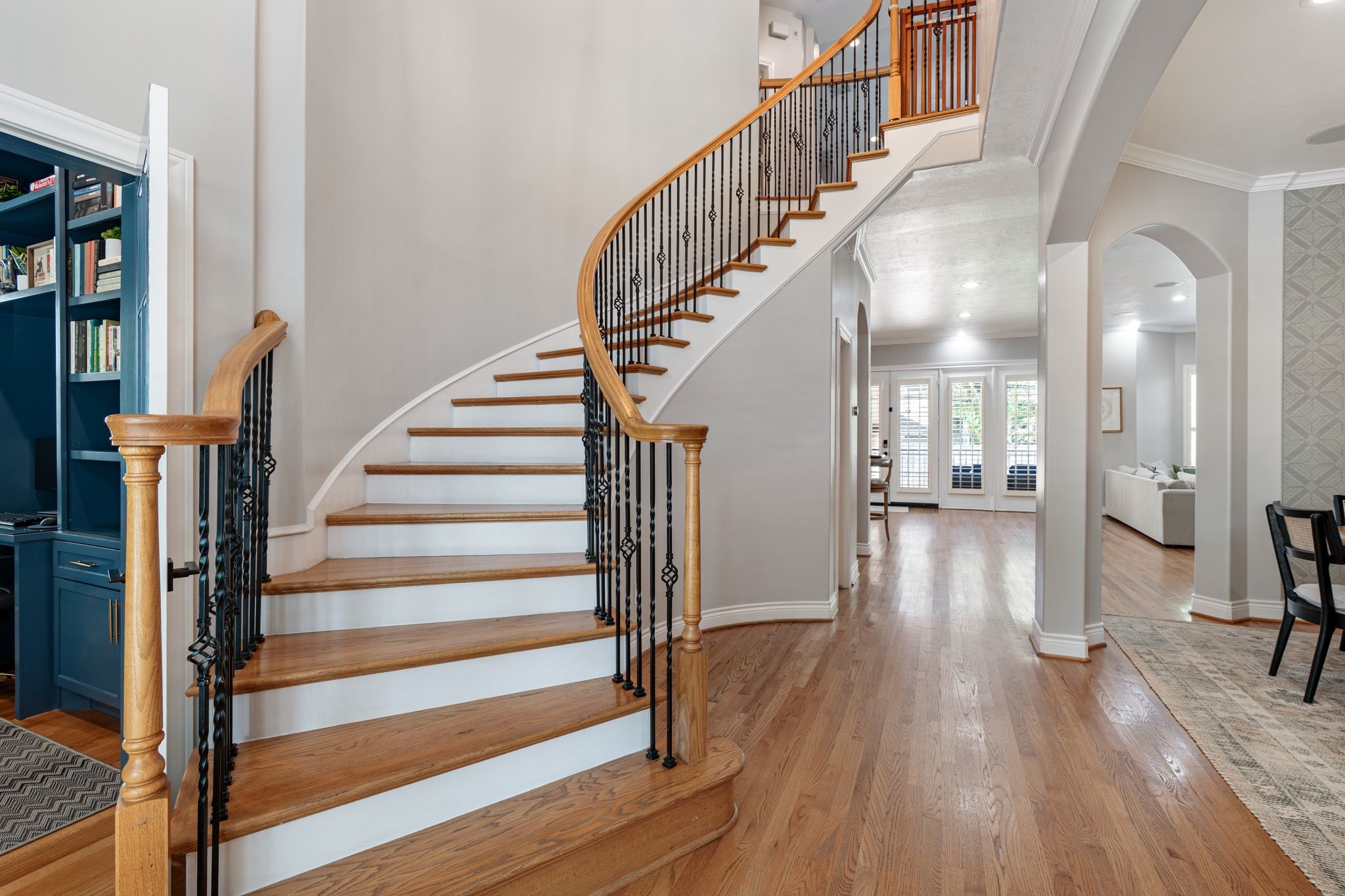 3822 Merrick Street Houston, TX 77025 - Photo 2 of 34 The showstopping curved staircase is the centerpiece of the entry hall, featuring stained oak treads with white painted risers, an oak handrail, and ornamental iron balusters with diamond detailing. The soaring two-story ceiling height and open sightlines through arched doorways to the living areas and formal dining room make this entry truly grand.