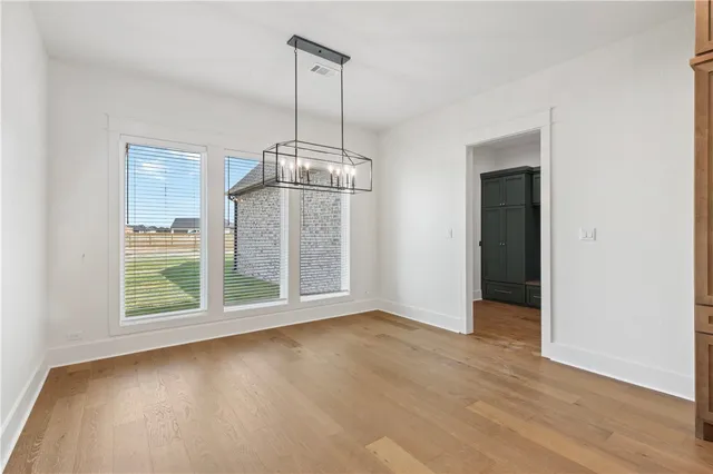 a view of an empty room with wooden floor kitchen view and a window