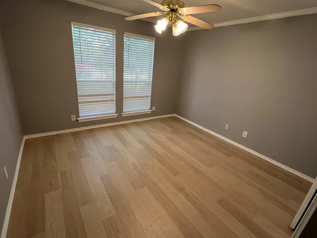 an empty room with wooden floor fan and windows