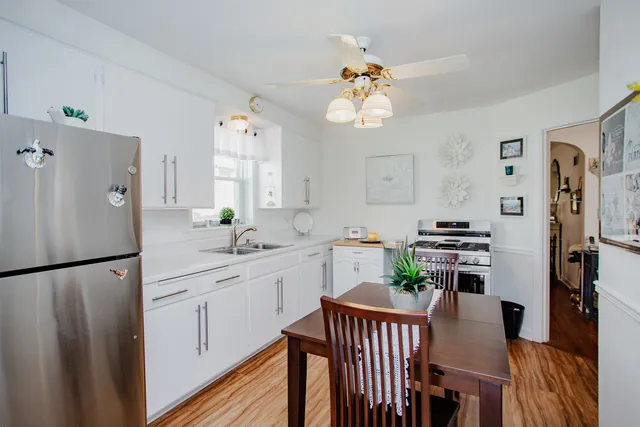 a kitchen with stainless steel appliances granite countertop a refrigerator a sink dishwasher and a dining table with wooden floor