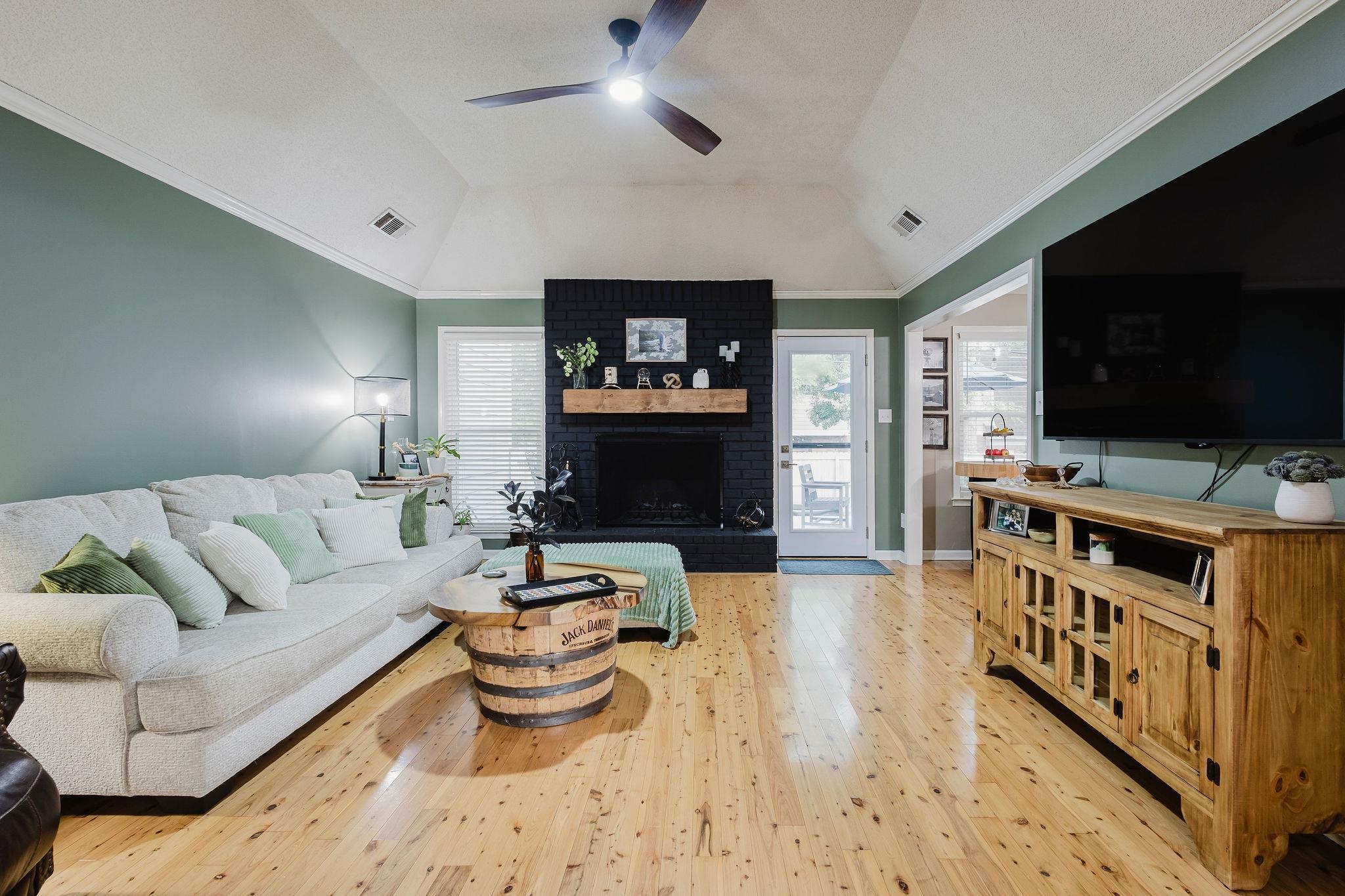305 Great Falls Road Collierville, TN 38017 - Photo 6 of 23 Vaulted ceiling living area featuring wood-finish flooring, a black brick fireplace with a wood mantel, and crown molding