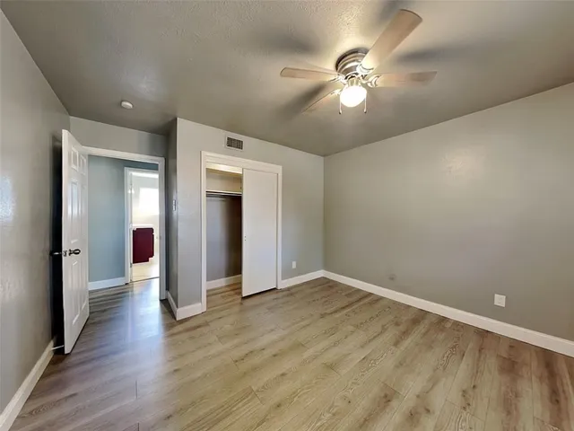 a view of an empty room with wooden floor and a ceiling fan