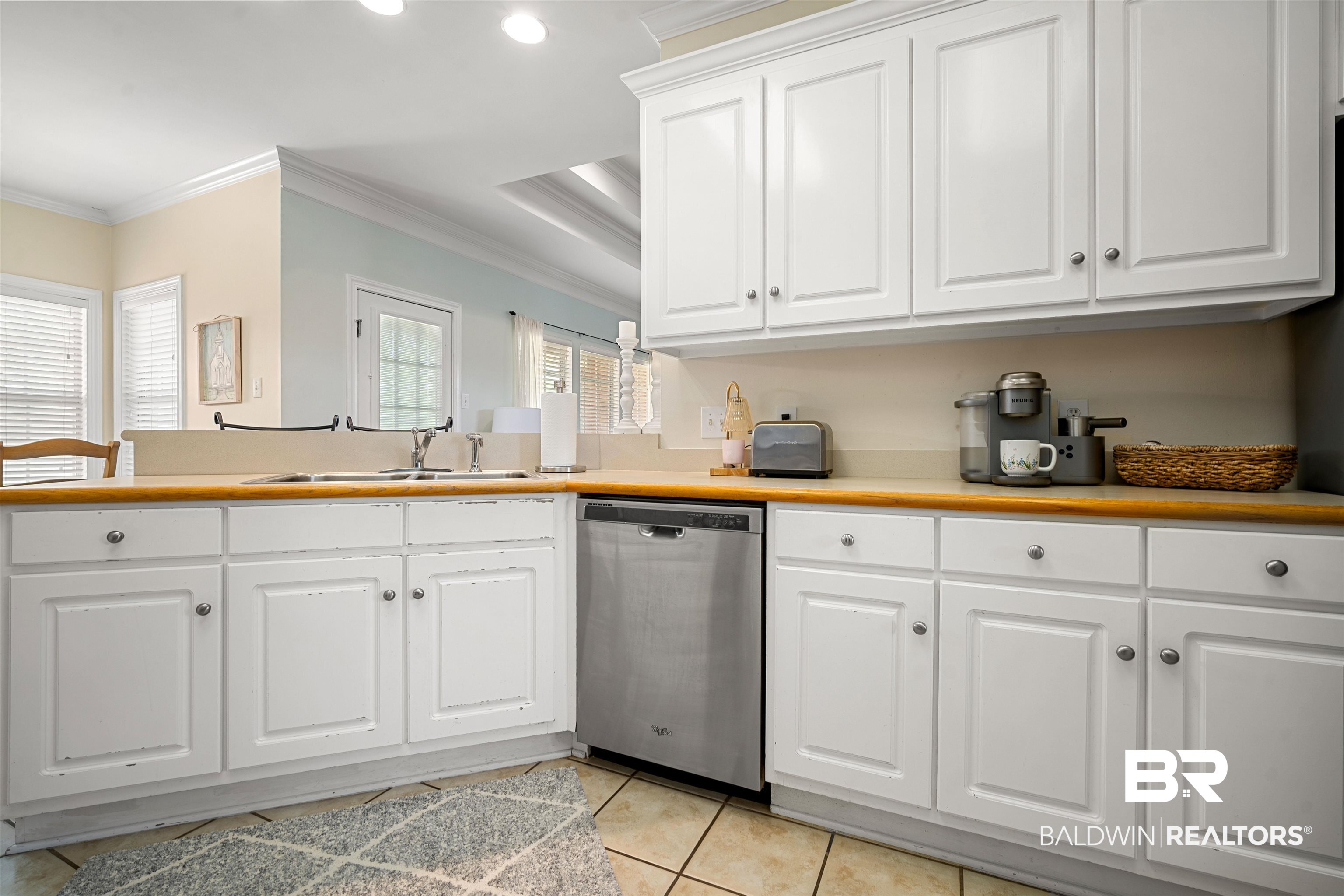9552 White Castle Road Mobile, AL 36695 - Photo 9 of 31 Kitchen with stainless steel dishwasher, light tile flooring, crown molding, and white cabinetry