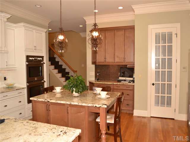 9009 Albatross Court Raleigh, NC 27613 - Photo 3 of 25 a kitchen with kitchen island granite countertop a stove a refrigerator a sink a dining table and chairs with wooden floor