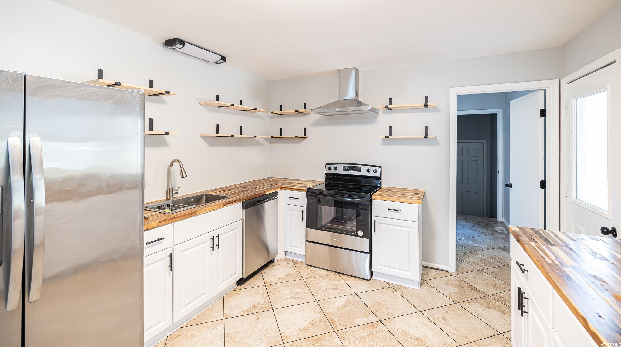 117 George Washington Trail Georgetown, SC 29440 - Photo 21 of 30 Kitchen with butcher block countertops, wall chimney range hood, sink, appliances with stainless steel finishes, and white cabinets