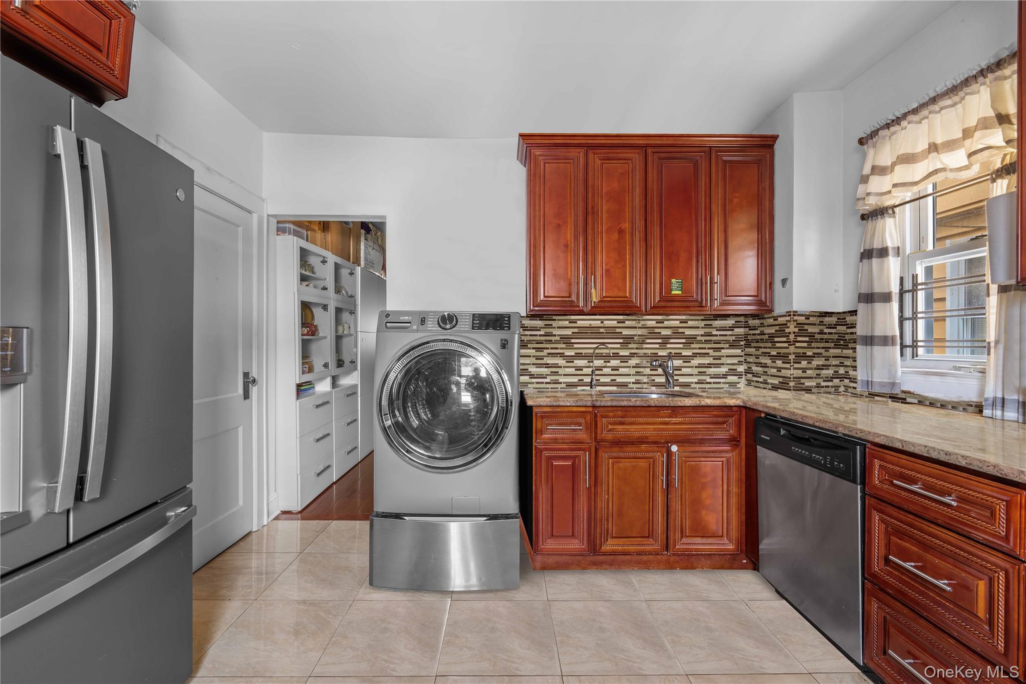 89-13 85th Street Queens, NY 11421 - Photo 5 of 15 Kitchen featuring appliances with stainless steel finishes, light stone countertops, tasteful backsplash, light tile patterned floors, and washer / clothes dryer