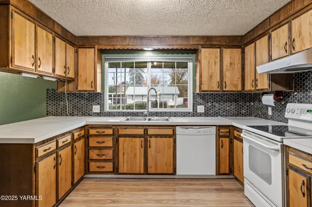 a kitchen with stainless steel appliances granite countertop a sink and wooden cabinets with a granite countertops next to a window