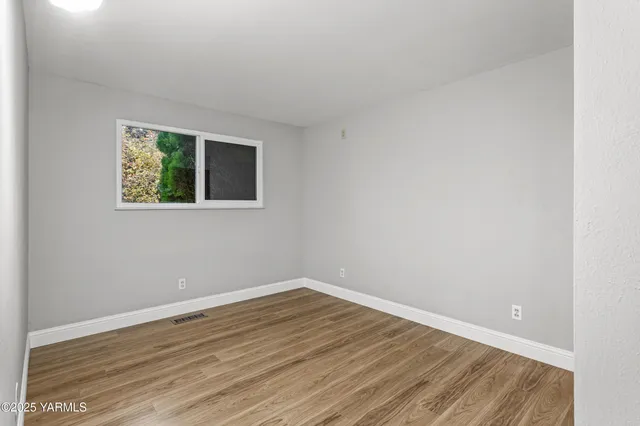a view of an empty room with wooden floor and closet