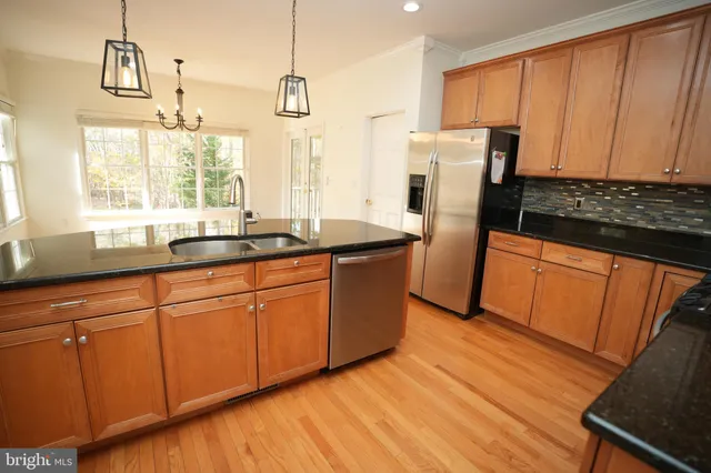 a kitchen with stainless steel appliances granite countertop a refrigerator a sink dishwasher and wooden cabinets with wooden floor