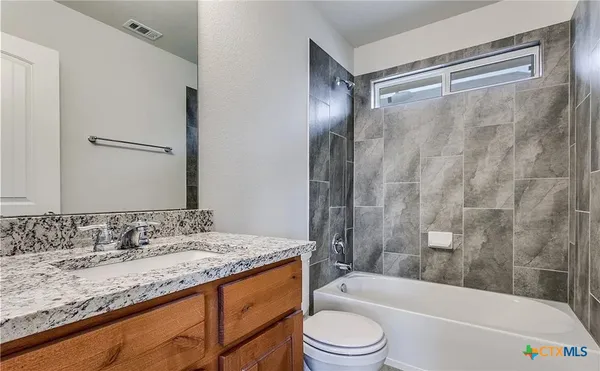 a bathroom with a granite countertop bathtub shower sink vanity and toilet