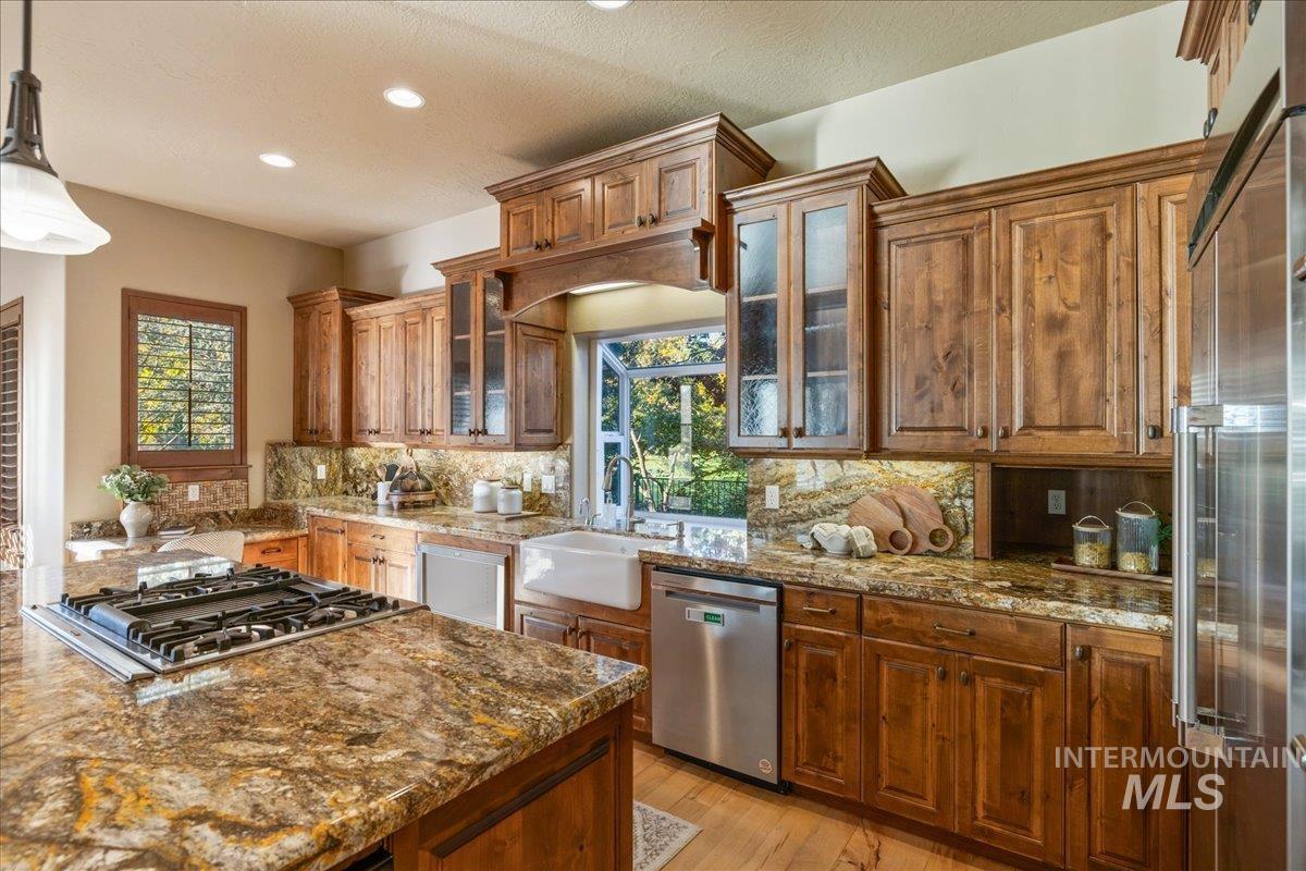 1479 West Oakhampton Drive Eagle, ID 83616 - Photo 11 of 49 Kitchen with dark stone countertops, light wood-style floors, appliances with stainless steel finishes, brown cabinetry, and healthy amount of natural light