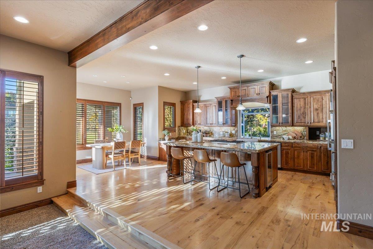1479 West Oakhampton Drive Eagle, ID 83616 - Photo 12 of 49 Kitchen with glass insert cabinets, brown cabinetry, beamed ceiling, a breakfast bar area, and decorative backsplash