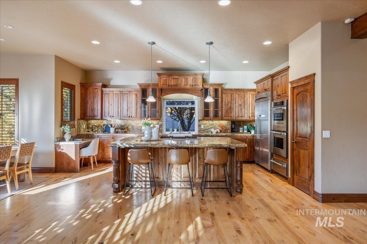 1479 West Oakhampton Drive Eagle, ID 83616 - Photo 13 of 49 Kitchen featuring brown cabinets, a kitchen island, tasteful backsplash, a breakfast bar area, and recessed lighting