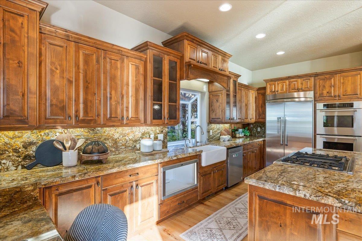 1479 West Oakhampton Drive Eagle, ID 83616 - Photo 10 of 49 Kitchen featuring brown cabinets, glass insert cabinets, appliances with stainless steel finishes, recessed lighting, and a textured ceiling