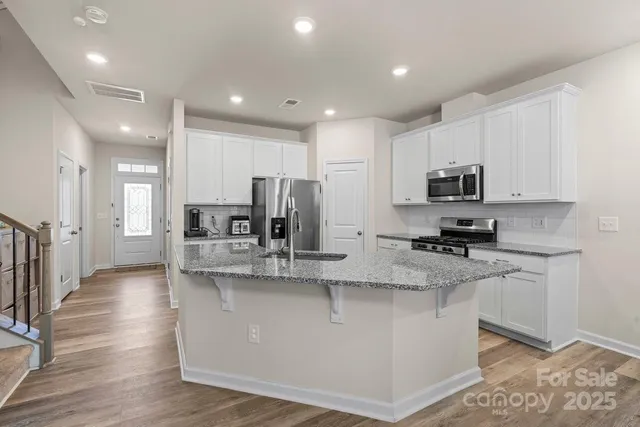 a large kitchen with stainless steel appliances granite countertop a stove a sink a refrigerator and white cabinets with wooden floor