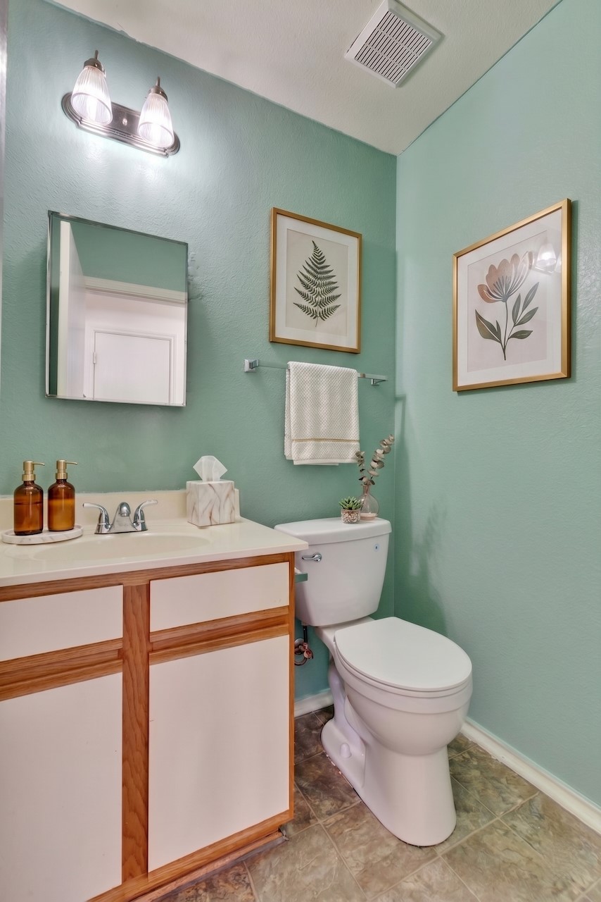 7504 Redrick Drive Austin, TX 78747 - Photo 12 of 34 The bathroom features a vanity with a white countertop and a mirror, a toilet, and a ceiling-mounted ventilation fan