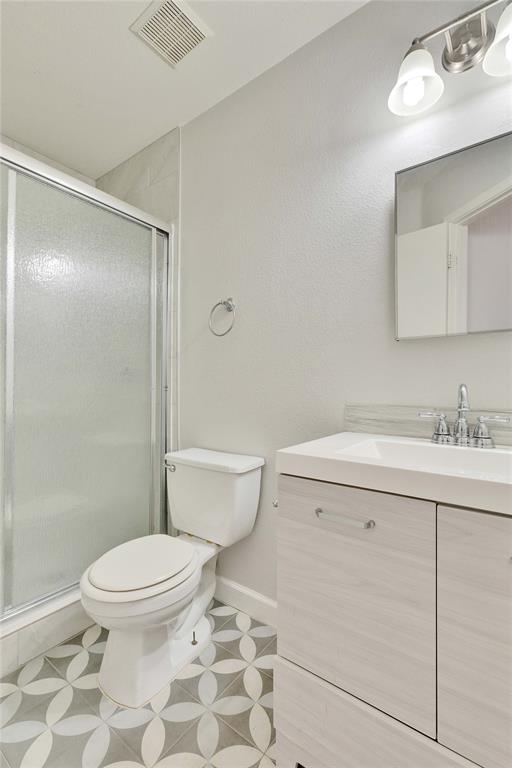 7504 Redrick Drive Austin, TX 78747 - Photo 25 of 34 Bathroom featuring a tiled shower, a toilet, a vanity with an integrated sink, and an overhead light fixture