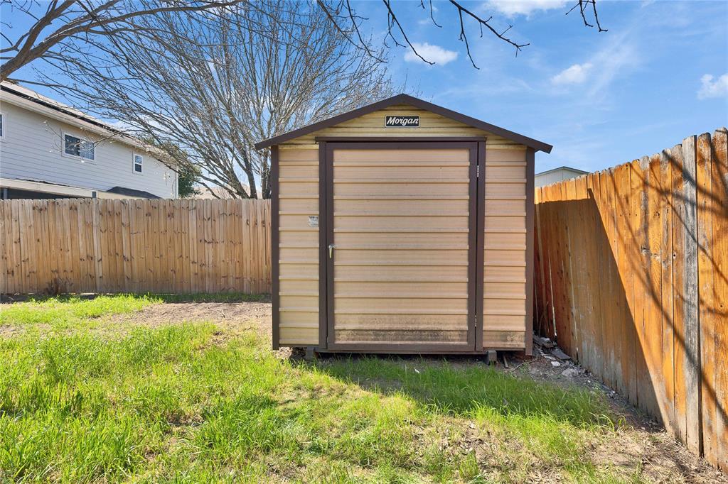 7504 Redrick Drive Austin, TX 78747 - Photo 33 of 34 The property includes a storage shed with a brown door, set within a yard featuring grass and a wooden fence